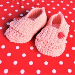 Paire de chaussons roses bébé crochetées main avec un bouton en forme de coeur rouge sur la languette 