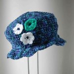 Chapeau enfant en fil de coton bleu violet et vert, deux fleurs coordonnées en guise de décoration avec une feuille.