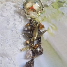 Broche Colombes aux plumages blancs avec des breloques filigranées gouttes et lisses, perles rondes et nœud en cristal, ruban organza crème, pendentif plaqué or avec un zircon sur une broche en métal